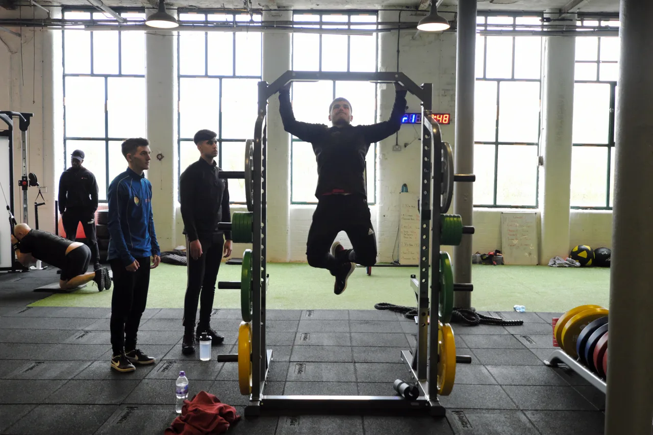 A PTNE tutor coaching two learners at the pull-up rack in a partner gym