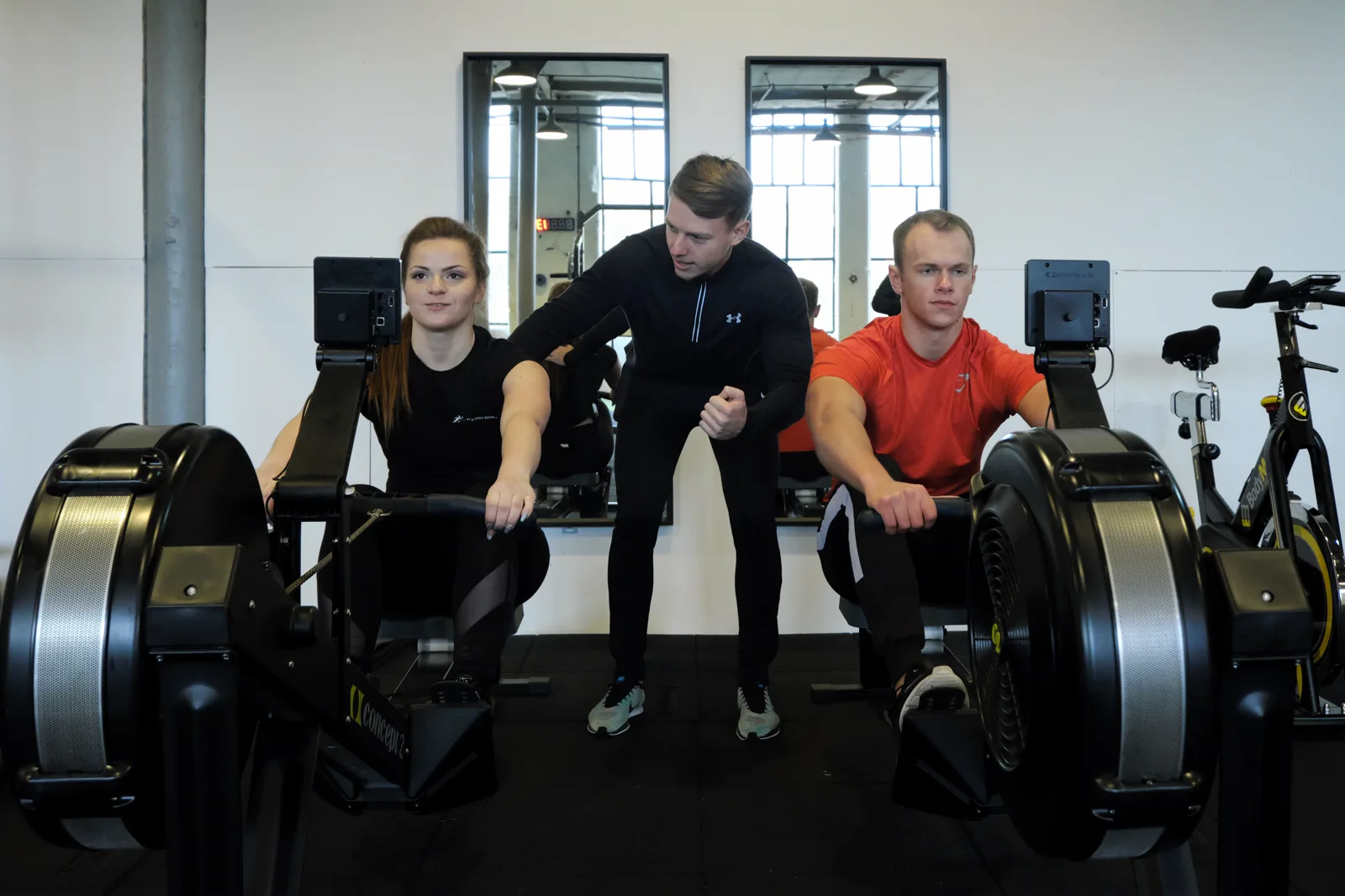 A PTNE coach leaning in to motivate two learners on rowing machines